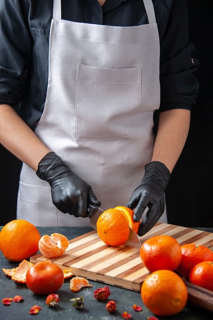 Vooraanzicht vrouwelijke kok die sinaasappel snijdt op donkere dranksalade gezondheidsmaaltijd voedsel plantaardig fruitdieet