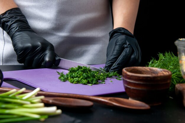 Vooraanzicht vrouwelijke kok die smakelijke salade maakt, snijgroenten op een donkere achtergrond keuken vakantie werk eten maaltijd baan kleur keuken