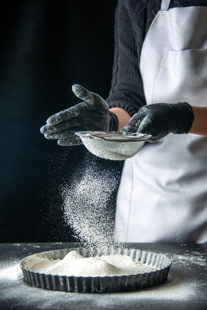 Vooraanzicht vrouwelijke kok die witte bloem in de pan giet op donkere eiercake bakkerij gebak keuken keuken deeg hotcake