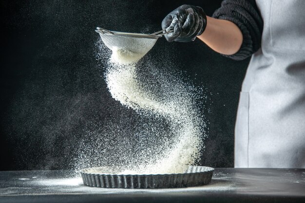 Vooraanzicht vrouwelijke kok die witte bloem in de pan giet op donkere eiercake bakkerij hotcake keuken keuken deegpastei