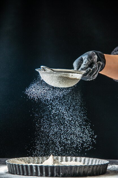 Vooraanzicht vrouwelijke kok die witte bloem in de pan op een donkere eiercake giet, bakkerijgebak, keukenkeuken, deegtaart, hotcake