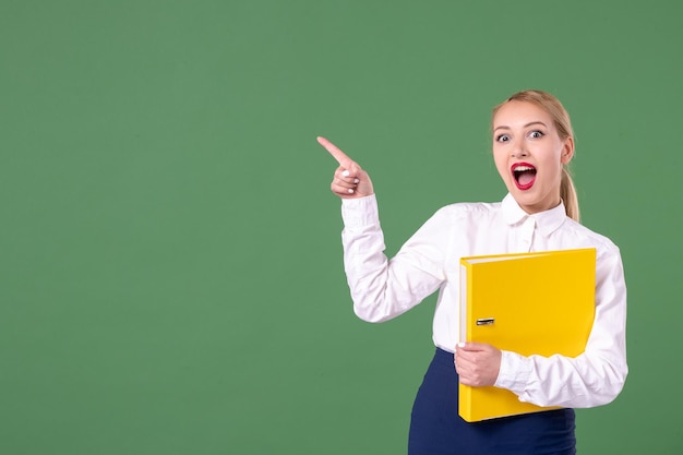 Vooraanzicht vrouwelijke leraar met gele bestanden op groene achtergrond les werk student universiteit studie uniform vrouw schoolboek