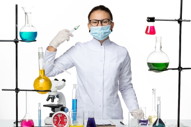 Vooraanzicht vrouwelijke scheikundige in medisch pak met injectie van de maskerholding op lichte witte achtergrond het laboratoriumcovidplons van het viruschemie