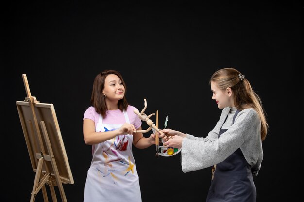 Vooraanzicht vrouwelijke schilders tekening afbeelding van menselijke figuur op ezel op zwarte muur tekenen schilderij kunst kunstenaar kleuren baan foto foto