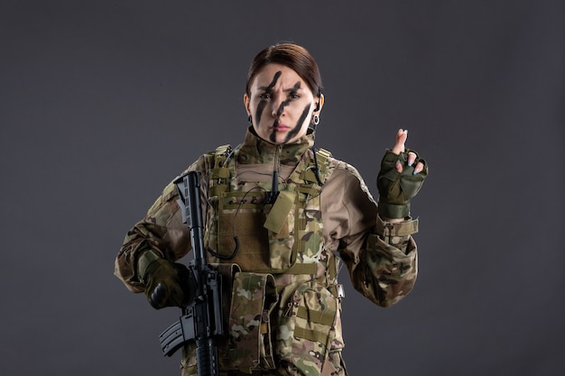 Vooraanzicht vrouwelijke soldaat met machinegeweer in camouflage op donkere muur