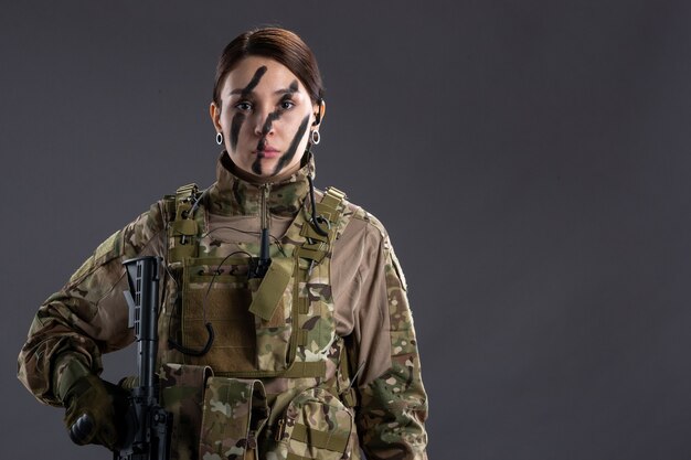Vooraanzicht vrouwelijke soldaat met machinegeweer in camouflage op grijze muur