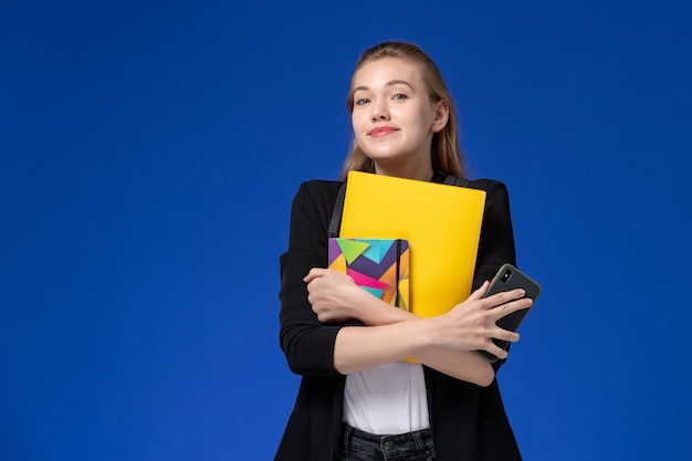 Vooraanzicht vrouwelijke student in zwart jasje rugzak houden bestand en voorbeeldenboek op blauwe muur boeken school college universitaire les