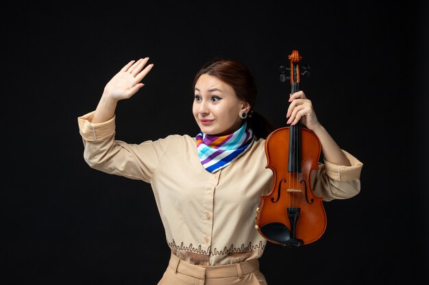 Vooraanzicht vrouwelijke violiste die haar viool houdt die op donkere muur zwaait concert melodie instrument vrouw prestatie muziek emotie spel