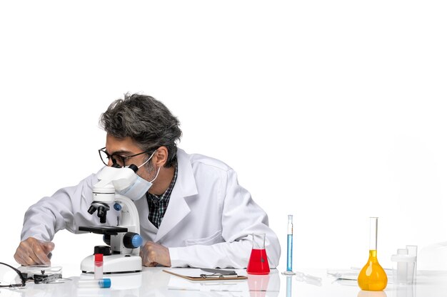Vooraanzicht wetenschapper van middelbare leeftijd in speciaal wit pak met behulp van Microscoop