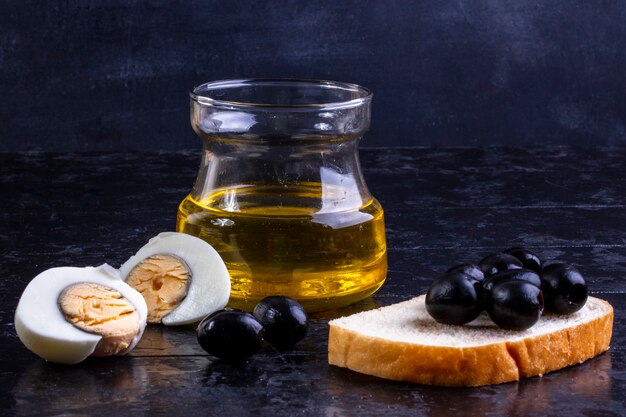 vooraanzicht zwarte olijven op sneetje brood met gekookt ei en olijfolie in een pot op zwart