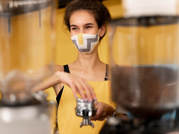 Gratis foto vooraanzichtbarista die een gezichtsmasker draagt tijdens het maken van koffie