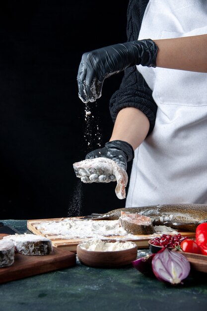 Vooraanzichtchef-kok die rauwe visplakken bedekt met bloem op de keukentafel