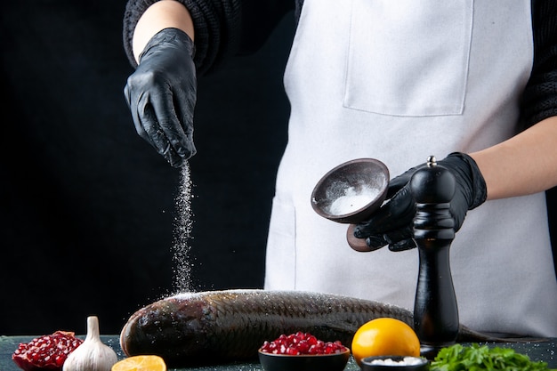 Vooraanzichtchef-kok met handschoenen besprenkeld zout op verse visgranaatappelzaden in kom op tafel Gratis Foto