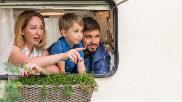 Vooraanzichtfamilie die uit het raam van een caravan met exemplaarruimte kijkt