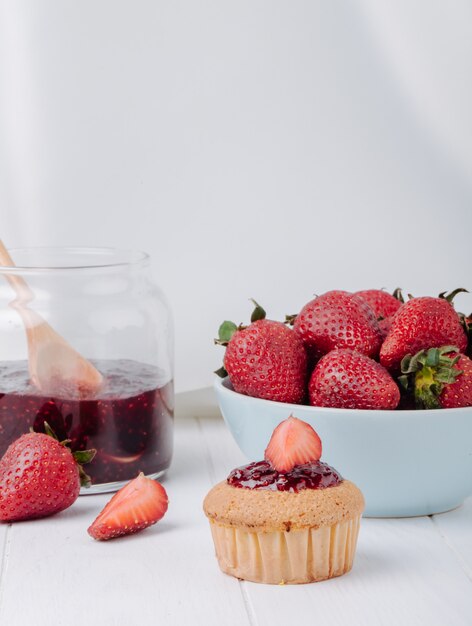 Vooraanzichtmuffin met aardbeien in een kom en frambozenjam in een kruik