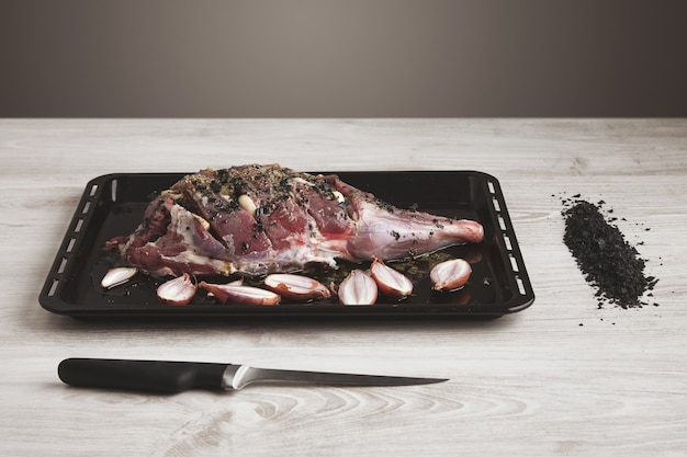 Voorgekookt IJslands lamsboutvlees met kruiden en specerijen en kleine uien op zwarte ovenschaal