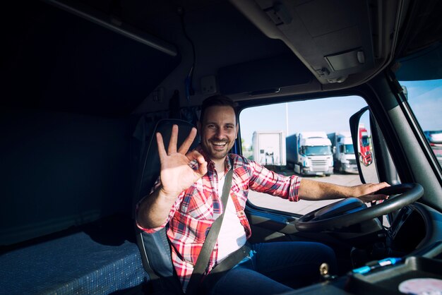 Vrachtwagenchauffeur houdt van zijn werk en toont ok gebaar terwijl hij in zijn vrachtwagencabine zit