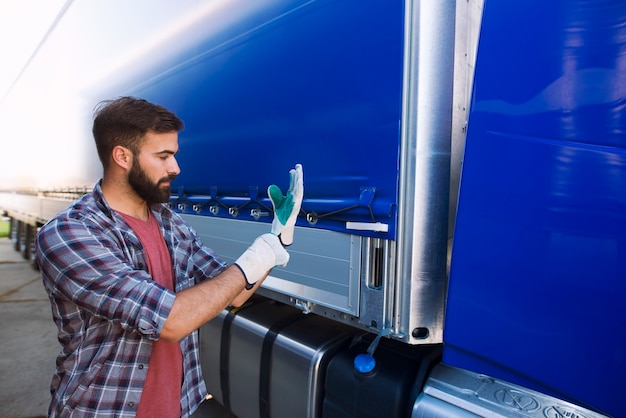 Vrachtwagenchauffeur trekt handschoenen aan om het dekzeil van het voertuig te verwijderen voor het lossen