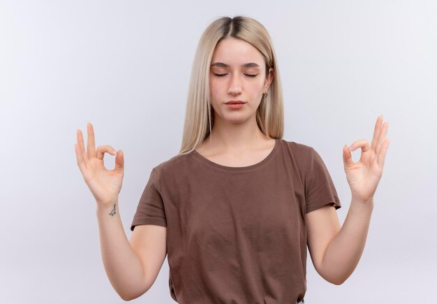 Vreedzaam jong blondemeisje die met gesloten ogen op geïsoleerde witte ruimte mediteren