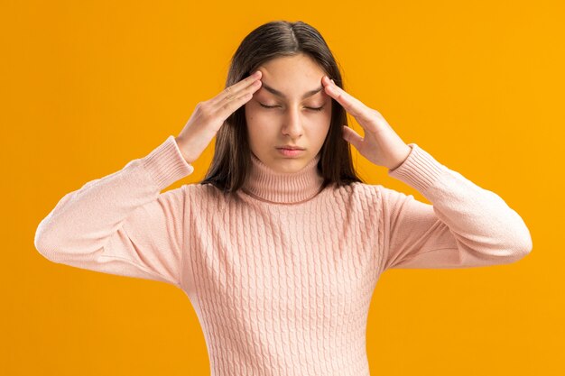 Vreedzaam mooi tienermeisje trekt wenkbrauwen op met gesloten ogen geïsoleerd op oranje muur