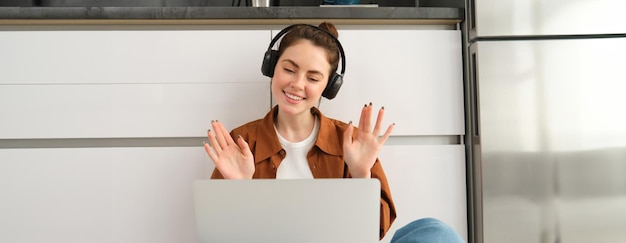 Gratis foto vreugdevolle jonge vrouw met koptelefoon zwaait met haar handen naar de laptop, sluit zich aan bij een online chat, verbindt zich met een externe cursus