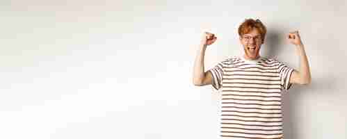 Gratis foto vreugdevolle roodharige man die zijn handen opsteekt als winnaar die een prijs wint en viert dat hij schreeuwt van vreugde