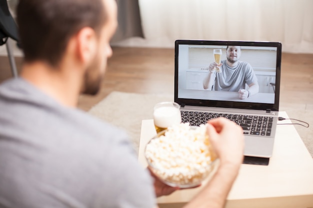 Vriend die bier drinkt en popcorn eet tijdens een videogesprek tijdens quarantaine.
