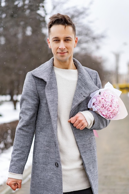 Vriend met een boeket roze bloemenhortensia die buiten op zijn vriendin wacht terwijl de sneeuw valt. Valetnine's dagconcept, huwelijksaanzoek man gaat op een date.