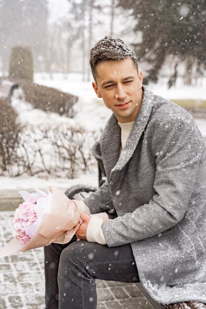 Vriend met een boeket roze bloemenhortensia die buiten op zijn vriendin wacht terwijl de sneeuw valt. Valetnine's dagconcept, huwelijksaanzoek man gaat op een date.