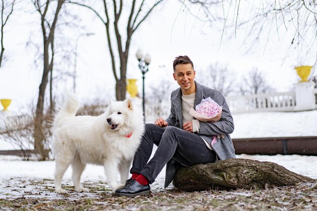 Vriend met een boeket roze bloemenhortensia die op zijn vriendin wacht en met een hond loopt en speelt. buiten terwijl er sneeuw valt. Valetnine's dagconcept, huwelijksaanzoek man gaat