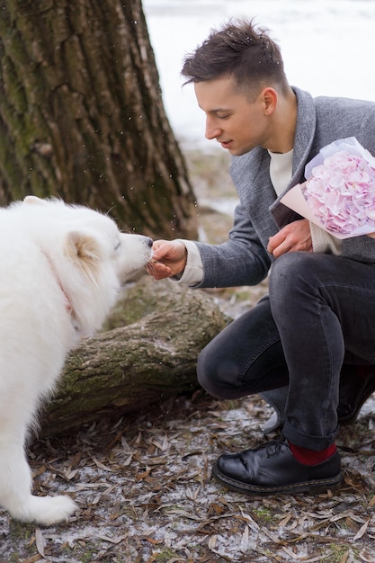 Gratis foto vriend met een boeket roze bloemenhortensia die op zijn vriendin wacht en met een hond loopt en speelt. buiten terwijl er sneeuw valt. valetnine's dagconcept, huwelijksaanzoek man gaat