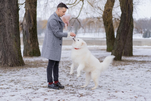 Vriend met een boeket roze bloemenhortensia die op zijn vriendin wacht en met een hond loopt en speelt. buiten terwijl er sneeuw valt. Valetnine's dagconcept, huwelijksaanzoek man gaat