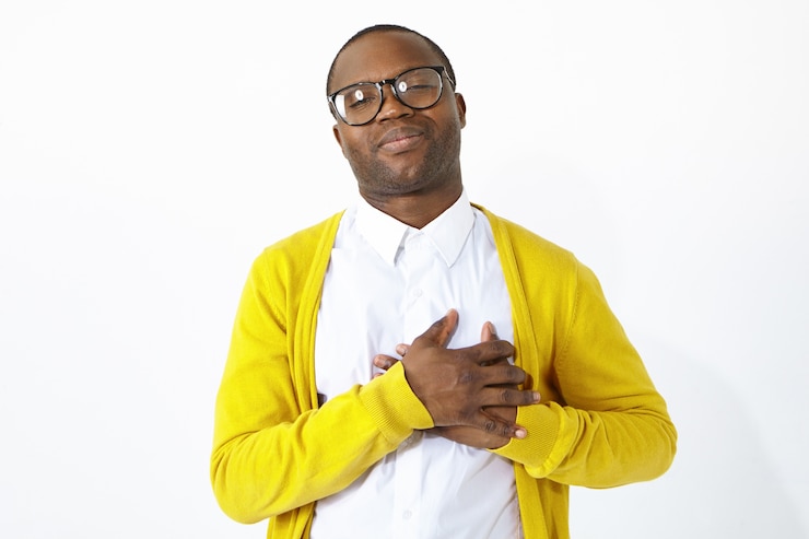 Gratis Foto vriendelijk ogende dankbare afro-amerikaanse man die de handen op zijn borst houdt, medeleven, erkenning en dankbaarheid toont, opgewekt of gevleid is. positieve menselijke emoties en lichaamstaal