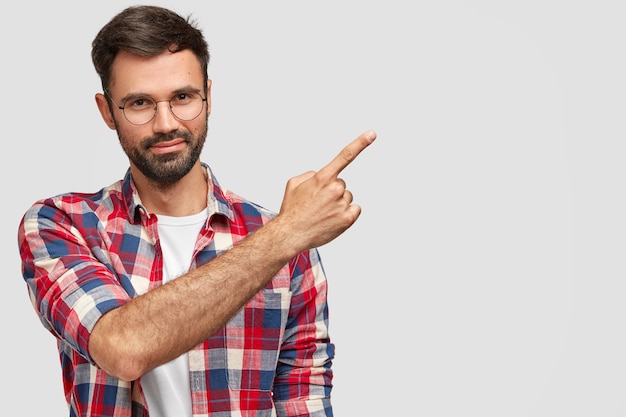 Vriendelijk ogende mannelijke verkoper met varkenshaar, gekleed in modieuze kleding, wijst naar de rechterbovenhoek