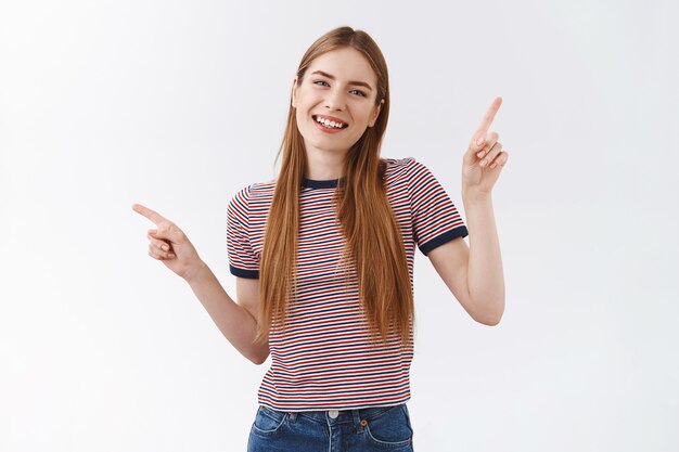 Vriendelijke, aangename vrolijke vrouw in gestreept t-shirt met lang blond haar, handen opzij wijzend, links en rechts keuzes laten zien, opgetogen glimlachen, suggesties geven