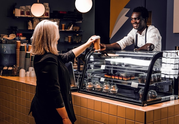 Vriendelijke Afrikaanse barista geeft de bestelde koffieklant van moderne coffeeshop