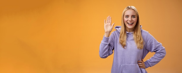 Gratis foto vriendelijke, energieke, behulpzame, charmante studente zegt hallo nieuwkomers zwaaiend met opgeheven handpalm hey hi ges