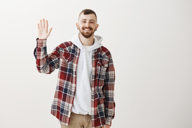 Vriendelijke gelukkige hipster kerel zwaaiende opgeheven hand om hallo te zeggen, je groeten