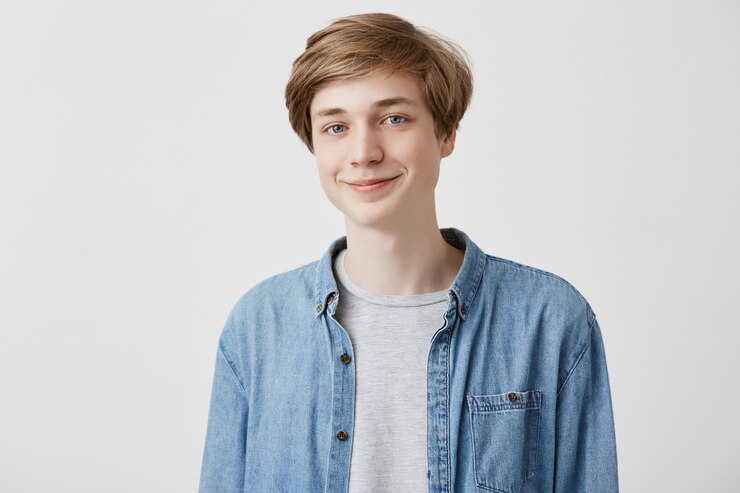 Gratis Foto vriendelijke jonge man glimlacht om goede grap, heeft blond haar en blauwe ogen, nonchalant gekleed, kijkt met tevreden uitdrukking, verheugt zich over succes als gelukkige student. mensen en positiviteitsconcept