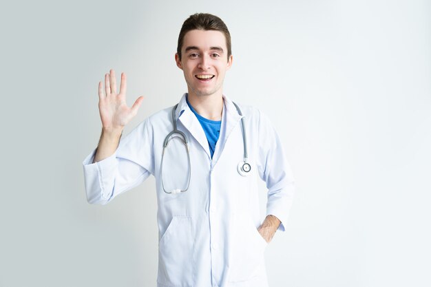 Vriendelijke jonge mannelijke arts zwaaiende hand