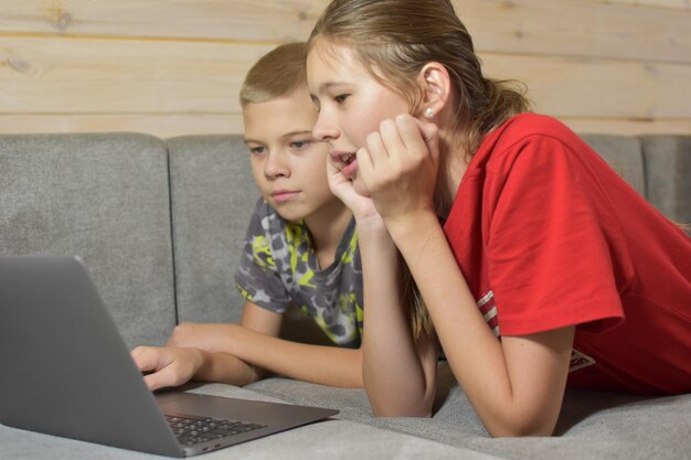 Vriendelijke kinderen liggen thuis op de bank video te kijken op een laptop. online afstandsonderwijs vanuit huis