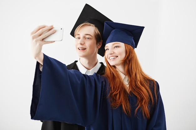 Vrienden afgestudeerden van de universiteit in caps glimlachen maken selfie.