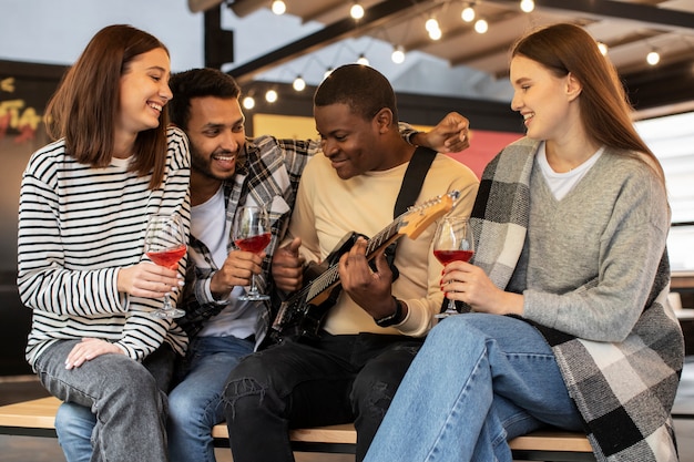 Vrienden die drankjes vasthouden terwijl ze luisteren naar hun vriend die gitaar speelt