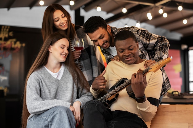 Vrienden die plezier hebben terwijl ze luisteren naar hun vriend die gitaar speelt