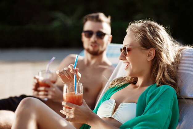 Vrienden glimlachen, cocktails drinken, liggend op ligstoelen bij zwembad