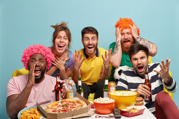 Vrienden, home entertainment, vrije tijd concept. Emotionele multi-etnische beste vrienden genieten van streaming tv, verbonden met draadloos internet, eten een snack en popcorn, geabonneerd op kabel of satelliet