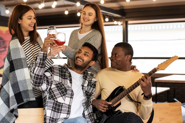 Vrienden juichen glazen wijn toe terwijl ze luisteren naar hun vriend die gitaar speelt