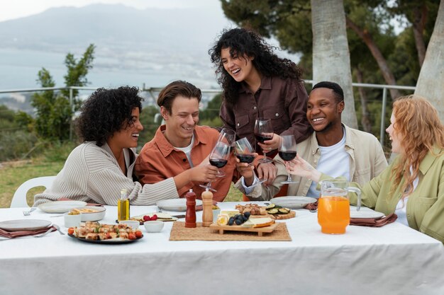 Vrienden roosteren met glazen wijn en barbecue eten tijdens buitenfeest