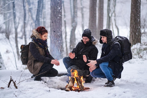 Vrienden wandelen in het besneeuwde bos. Jonge wandelaars verwarmd door het vuur.