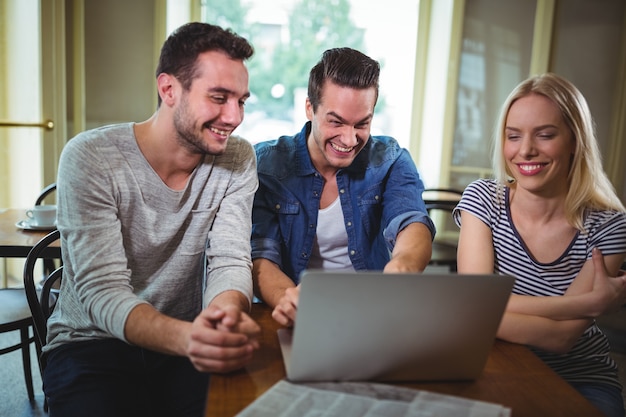 Vrienden zitten aan tafel en met behulp van laptop in cafÃ ©